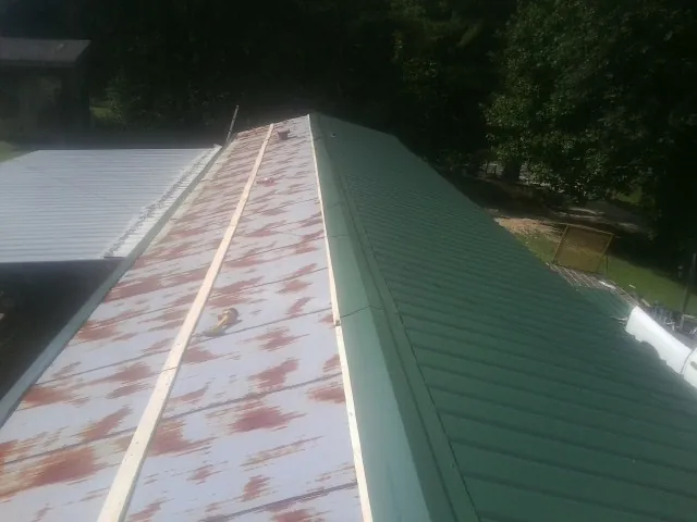 Old rusted panels beside newly installed green metal roofing — Wind Damage Roof Repair by Roofing Brothers in Brookville