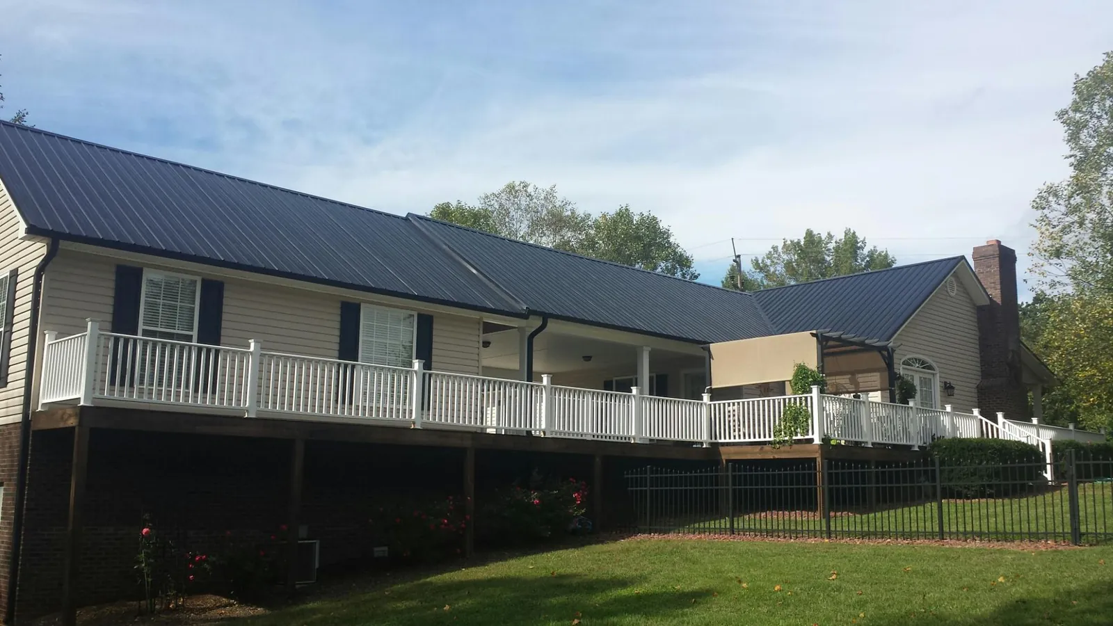 Black metal roof above a long white railed deck on a hillside home in Brookville