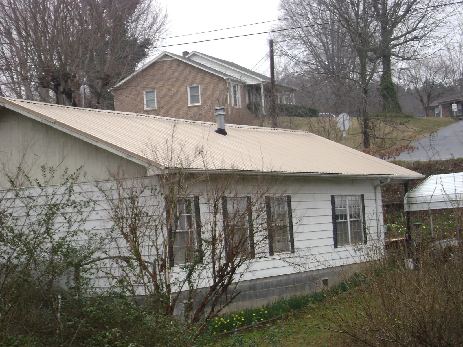 Tan metal roof on a white sided house set into a hillside — Commercial Roofing by Roofing Brothers in Brookville